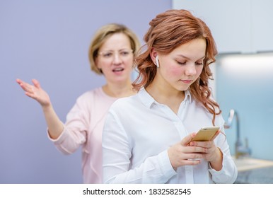 Mom scolds her teenage daughter while she ignores her while listening to music on the phone. Relationship problems with teenagers concept