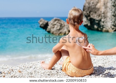 Mom smears her baby's back with sunscreen on a beach in Corfu, Greece. She draws a heart of cream on her son's back. 