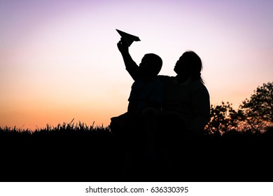 Mom And Son Child Playing With Paper Airplane In The Sunset