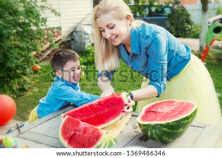 Mom and son cut a watermelon and laugh in the garden. Love and tenderness.