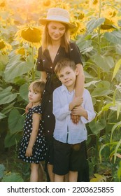 Mom, Son And Daughter In A Field Of Sunflowers In The Sun. Mother Mother Holding Son's Hand. Mom And Daughter Are Wearing Black Polka Dot Dresses. Sunlights In The Corner Of Photo.