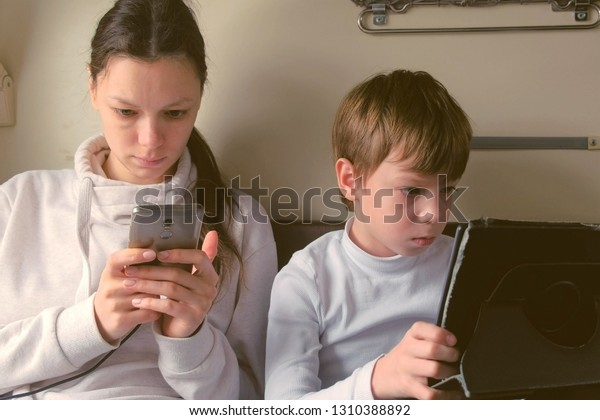Mom and son in gadgets travelling\
by train is playing a games in a second-class\
carriage.