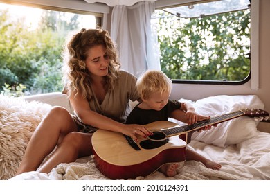 Mom And Son Have Fun In Camper Van. Young Family Relax Travelling Together By Caravan Car. Traveler Mother Teach Little Preschool Boy To Play Guitar In Motorhome. Adventures Vacation Recreational Trip