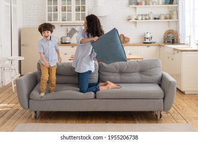 Mom and son have fun in living room fight with pillows together. Family leisure and recreation time. Cute cheerful and joyful young mother and little boy laugh while playing funny battle games at home - Shutterstock ID 1955206738