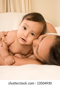 Mom And Son Lying Down On Bed And Mother Embracing The Infant Baby, Who Looks At Camera With Serious Facial Expression