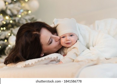 Mom And Son Are Lying On Bed In Bright Bedroom. Mum Kisses Baby. Woman Hugs Kid Boy Tightly. The Concept Of A Christmas Morning, Home Comfort, Scandy Style. Merry Christmas And Happy New Year.