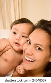 Mom And Son On Bed And Mother Embracing The Infant Baby, Who Looks Aside Of Camera With Serious Facial Expression