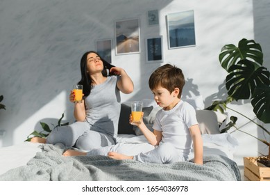 Mutter mit Sohn im Schlafanzug, der morgens im Bett Saft trinkt. 