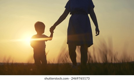 mom and son in the park. mom holding her son hand walking in the park silhouette at sunset in nature. lifestyle happy family kid dream concept. mom and son family walking in nature - Powered by Shutterstock