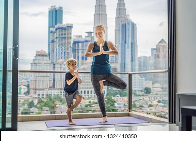 Mom and son are practicing yoga on the balcony in the background of a big city. Sports mom with kid doing morning work-out at home. Mum and child do the exercises together, healthy family lifestyle