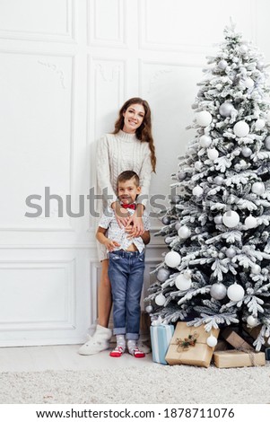 Mom and son sit by Christmas tree presents lights garland new year