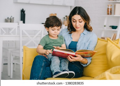 Mom And Son Sitting On Yellow Sofa And Reading Book