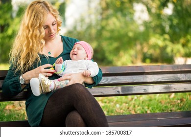 Mom Soothes A Crying Baby, Sitting On A Park Bench 