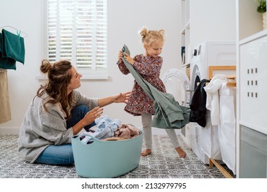 Mom spends time with daughter in bathroom, laundry room while doing daily chores, girl takes things out of washing machine and hands to woman who puts colorful clean clothes into bowl
