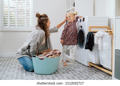 Mom Spends Time With Daughter In Laundry Room While Doing Daily Chores Girl Has Taken All Clean Clothes Out Of Washing Machine She Stands Proudly With Smile Woman Praises Child Strokes Her Head