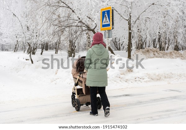 Mom with a\
stroller crosses the road in\
winter