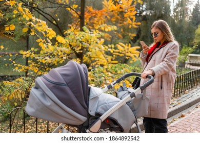 Mom With Stroller Walks In The Park And Texting On The Phone. Smartphone Addiction Concept