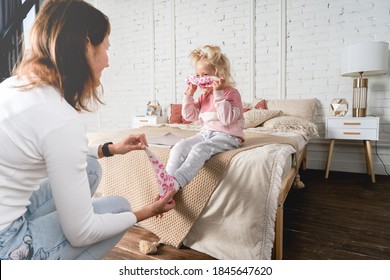 Mom takes off her little daughter's socks and tickles her feet a little. The girl laughs.
