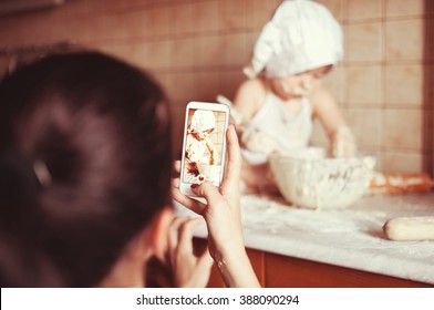 Mom Takes Photos With Her Phone Like A Little Boy Playing With A Fry Test On The Table In An Apron And Chef's Hat