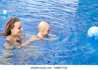 Mom Teaches A Child To Swim. Coach Teaches Toddler To Swim In The Pool. They Play With A Ball.