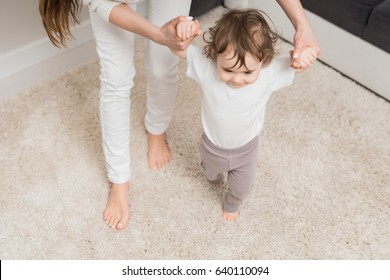 Mom Teaches Her Daughter To Walk. Helps And Supports The Child Learning To Walk. The Child Enjoys The First Steps.