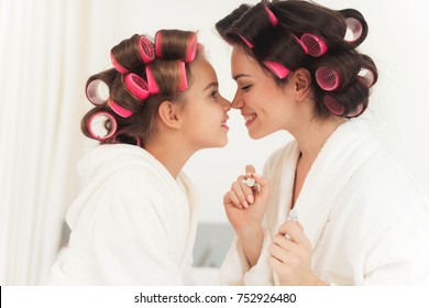 Mom teaches a little daughter to do makeup. They sit in their white bathrobes on the bed in their bedroom. On their heads they have curlers. - Powered by Shutterstock