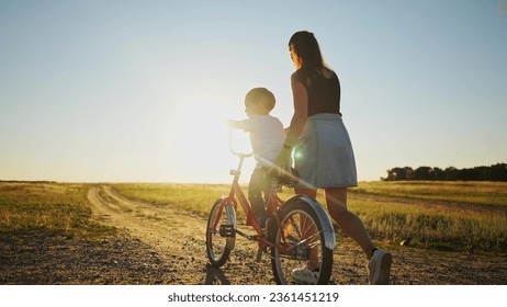 mom teaches son to ride bike. happy family childhood dream concept. mom and little son learn to ride a bike silhouette in the park in sunlight nature. happy family goes in for sports outdoors - Powered by Shutterstock