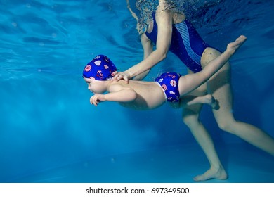 Mom teaches son to swim underwater in the pool on a blue background. Portrait. The view from under the water. Landscape orientation