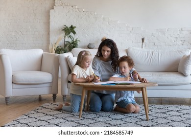 Mom teaching cute daughter   son kids to draw in colorful pencils in paper album  sitting at small table heating floor in living room  enjoying creative process  playtime  family leisure