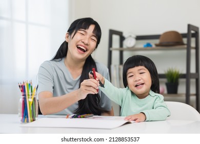 Mom teaching son how to painting and crayon color book doing homework  Happy asian boy painting and crayon   colored pencil and his mother in living room at home   family concept 
