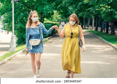 Mom And Teen Daughter Spend Time Together In The Park. People On A Walk In Disposable Masks.