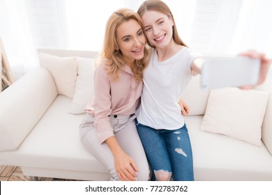 Mom And Teenage Daughter Do Selfie. They Are Sitting On The Couch At Home. They Are In A Good Mood. They Are Happy With Each Other.