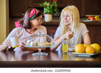 Mom And Teenage Daughter Eating Together, Sitting At Table At Home In Kitchen