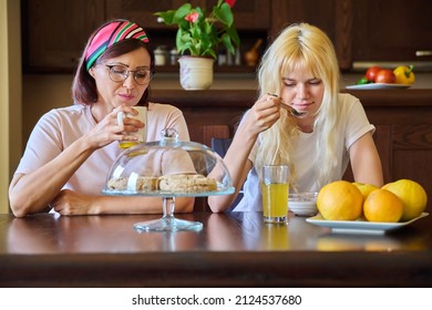 Mom And Teenage Daughter Eating Together, Sitting At Table At Home In Kitchen