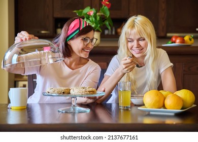 Mom And Teenage Daughter Eating Together, Sitting At Table At Home In Kitchen