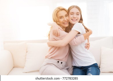 Mom And Teenage Daughter Embrace. They Are Sitting On The Couch At Home. They Are In A Good Mood. They Are Happy With Each Other.