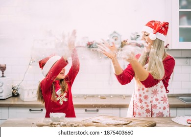 Mom And Teenage Daughter Are Playing In The Kitchen With Flour With Red Sweaters And A Santa Hat. Blurred Motion. Christmas Cooking Preparation Concept