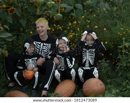Mom and three boys with pumpkins in carnival costumes of skeletons sit among the thickets of sunflower