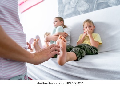 Mom tickles her son's bare heels. The boy is sitting on the sofa and laughing merrily.