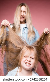 Mom Is Trying To Untangle Her Daughter's Long Blond Hair. The Child Does Not Want To Do A Hairstyle. Isolated On Pink Background.