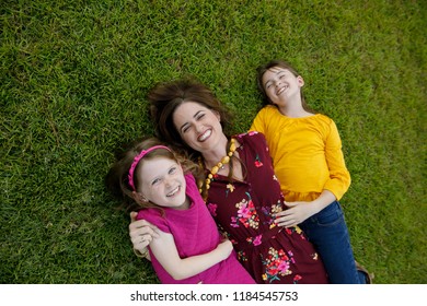 Mom And Two Daughters Laying On Ground Grass Being Silly Having Fun Laughing