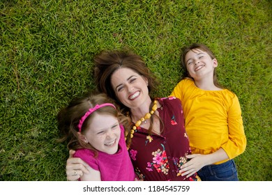 Mom And Two Daughters Laying On Ground Grass Being Silly Having Fun Laughing