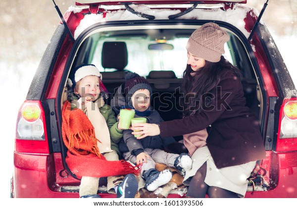 Mom and two sons in a car\
with hot coffee, a winter picnic with rugs and tea, a red car and\
snowfall