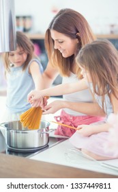 Mom With Two Young Twins Daughters In The Kitchen Cooking Spaghetti.