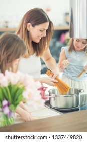 Mom With Two Young Twins Daughters In The Kitchen Cooking Spaghetti.