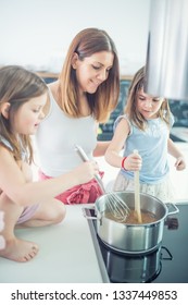 Mom With Two Young Twins Daughters In The Kitchen Cooking Spaghetti.