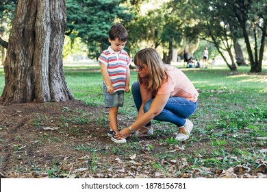 Mom Tying Sneakers To Her Little Son. Mother With Her Child In The Middle Of Forest Park.