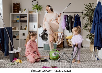 Mom Watches Daughters Clean With Girls In Bathroom, Laundry Room, Housekeeping. Woman Plays Mop Like Guitar, Listens To Music On Headphones, Sings, Concert While Cleaning.