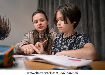 Mom watches as her child does her homework. Mom studies with her son at home. Home schooling.