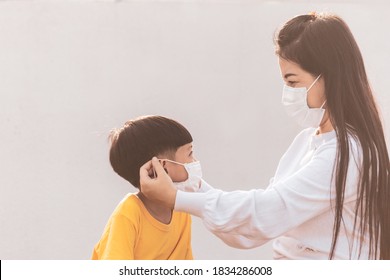 Mom Is Wearing A Medical Mask For Her Child. Little Asian Boy And Mom In Medical Mask. Asian Family Protection Virus Concept.